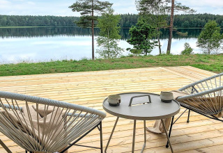Terrasse med moderne stole og bord, udsigt over fredfyldt sø og skov ved Cozy Sea House i Sverige.