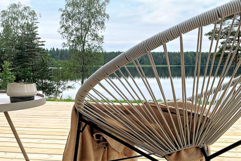 Udsigt fra træterrasse med moderne stol og bord, udsigt over sø og skov ved Cozy Sea House i Sverige.