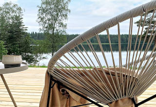 Udsigt fra træterrasse med moderne stol og bord, udsigt over sø og skov ved Cozy Sea House i Sverige.
