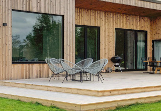 Træterrasse med moderne stole og grill udenfor Cozy Sea House med gæstehus i Sverige. Store vinduer.