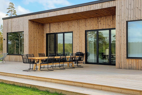 Udendørs træterrasse med spisebord og stole ved Cozy Sea House med Guest Cottage i Sverige, omgivet af natur.