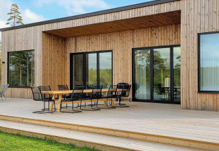 Udendørs træterrasse med spisebord og stole ved Cozy Sea House med Guest Cottage i Sverige, omgivet af natur.