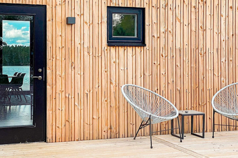 Træterrasse med moderne stole udenfor Cozy Sea House med Guest Cottage i Sverige, spejlingsvindue.