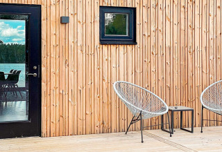 Træterrasse med moderne stole udenfor Cozy Sea House med Guest Cottage i Sverige, spejlingsvindue.