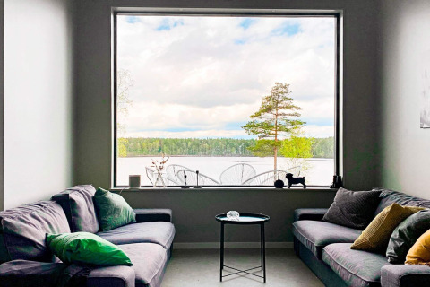 Stue i Cozy Sea House med udsigt til stor rude, sø, træer og skov i Sverige, moderne indretning.