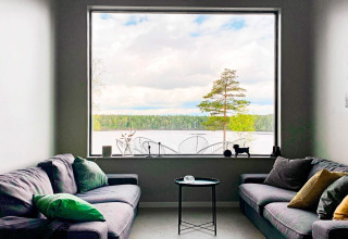 Stue i Cozy Sea House med udsigt til stor rude, sø, træer og skov i Sverige, moderne indretning.