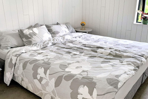 Dobbeltseng med gråt og hvidt blomstret sengetøj på Cozy Sea House med gæstehytte i Sverige.