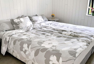 Dobbeltseng med gråt og hvidt blomstret sengetøj på Cozy Sea House med gæstehytte i Sverige.