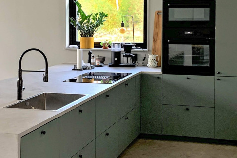 Moderne køkken i Cozy Sea House med grønne skabe, sort ovn og store vinduer, set i Sverige.