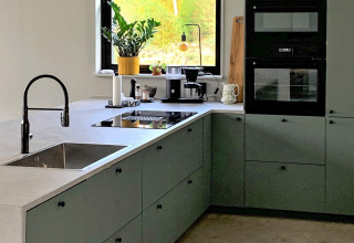 Moderne køkken i Cozy Sea House med grønne skabe, sort ovn og store vinduer, set i Sverige.