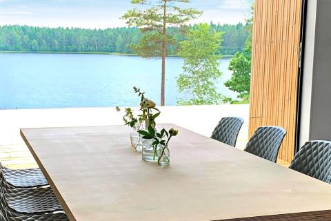 Spisebord med blomster og udsigt over en sø og skov ved Cozy Sea House med gæstehytte i Sverige.