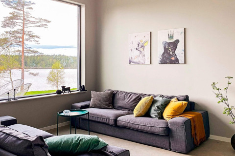 Stue med store vinduer, udsigt til sø og skov, moderne sofa og dyreillustrationer, Sverige.