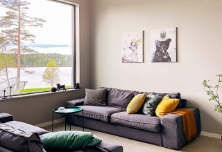 Stue med store vinduer, udsigt til sø og skov, moderne sofa og dyreillustrationer, Sverige.