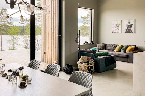 Moderne lodge i Sverige med stilfuld stue og spiseområde, store vinduer og udsigt over sø og skov.