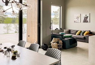 Moderne lodge i Sverige med stilfuld stue og spiseområde, store vinduer og udsigt over sø og skov.