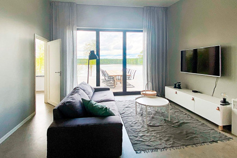 Lys stue i Cozy Sea House i Sverige med sofa, tv og udsigt til udendørs terrasse og natur.