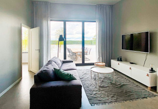 Lys stue i Cozy Sea House i Sverige med sofa, tv og udsigt til udendørs terrasse og natur.