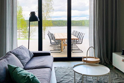 Stue med stor glasdør, der åbner ud til terrasse med søudsigt ved Cozy Sea House med gæstehytte i Sverige.