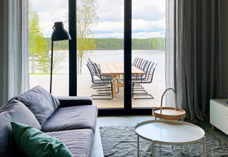 Stue med stor glasdør, der åbner ud til terrasse med søudsigt ved Cozy Sea House med gæstehytte i Sverige.
