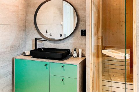 Moderne badeværelse med sort håndvask, rund spejl og glasdør til sauna på Cozy Sea House i Sverige.