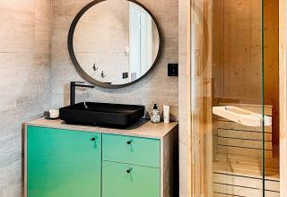 Moderne badeværelse med sort håndvask, rund spejl og glasdør til sauna på Cozy Sea House i Sverige.