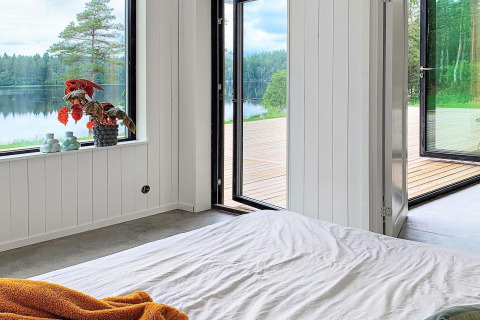 Soveværelse i Cozy Sea House i Sverige med udsigt til sø, træer og en åben terrasse, minimalistisk stil.