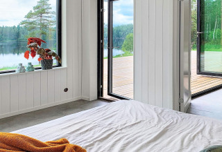 Soveværelse i Cozy Sea House i Sverige med udsigt til sø, træer og en åben terrasse, minimalistisk stil.