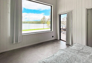 Soveværelse i Cozy Sea House med udsigt til sø og skov gennem store vinduer, Sverige.