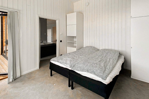 Soveværelse i Cozy Sea House med enkeltsenge, hvid trævæg, minimalistisk design og udsigt til terrasse.
