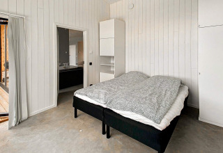 Soveværelse i Cozy Sea House med enkeltsenge, hvid trævæg, minimalistisk design og udsigt til terrasse.