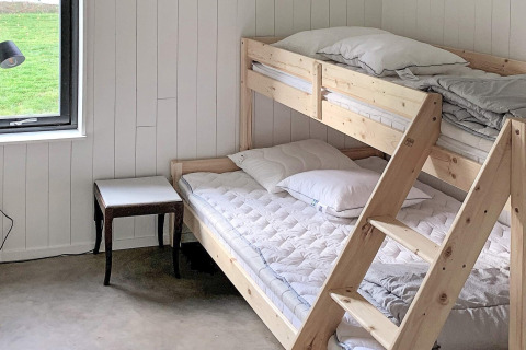 Et lyst værelse i Cozy Sea House med køjesenge i træ, et lille bord og udsigt til en grøn græsplæne i Sverige.