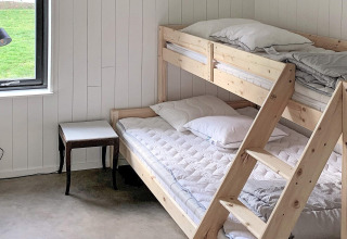 Et lyst værelse i Cozy Sea House med køjesenge i træ, et lille bord og udsigt til en grøn græsplæne i Sverige.
