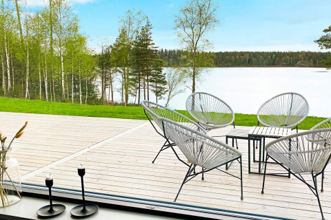 Udsigt fra Cozy Sea House i Sverige med moderne havestole på en træterrasse, sø og skov i baggrunden.