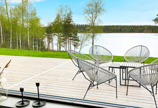 Udsigt fra Cozy Sea House i Sverige med moderne havestole på en træterrasse, sø og skov i baggrunden.