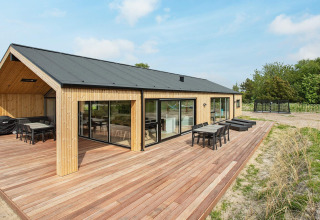 Moderne feriebolig i Sæby, Danmark, med træbeklædning, stor terrasse og havemøbler i naturskønne omgivelser.