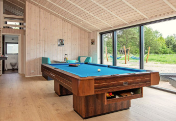 Table de billard dans un salon lumineux avec grandes baies vitrées, vue nature, maison de vacances Sæby.