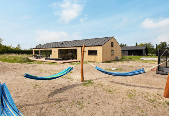 Buitenaanzicht van een modern vakantiehuis voor 10 personen in Sæby met hangmatten en zandtuin.
