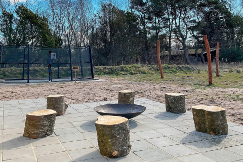 Buiten vuurplaats met boomstamzitjes en trampoline bij 10-persoons vakantiewoning in Sæby, Denemarken.