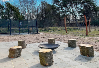 Buiten vuurplaats met boomstamzitjes en trampoline bij 10-persoons vakantiewoning in Sæby, Denemarken.
