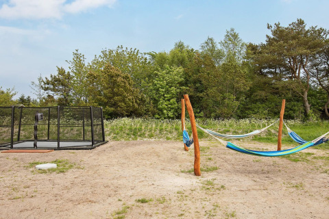 Udendørs legeplads i Sæby, Danmark, med hængekøjer og trampolin omgivet af grøn natur ved feriehus.