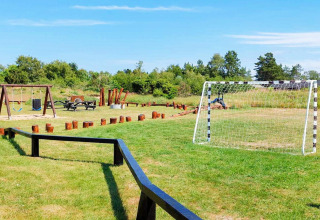 Udendørs legeplads med fodboldmål, gynger, bordbænkesæt og træstubbe ved feriebolig i Sæby, Danmark.