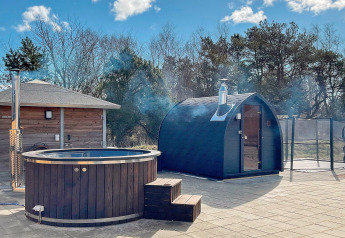 Spa extérieur et sauna près d’une maison de vacances à Sæby, Danemark, entourés d’arbres et de ciel bleu.