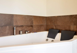 Bañera de hidromasaje de esquina con dos reposacabezas en casa vacacional en Sæby, Dinamarca, con azulejos marrones.