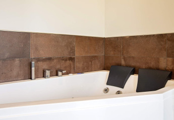 Bain à remous d’angle moderne avec deux appuie-têtes dans une maison de vacances à Sæby, Danemark, carrelage marron.