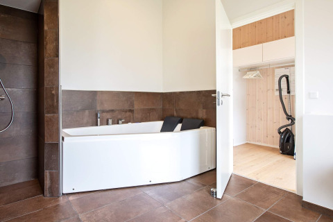 Baño moderno con bañera y armario abierto en una casa de vacaciones para 10 personas en Sæby, Dinamarca.