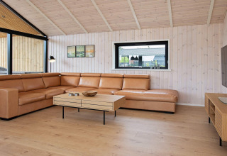 Moderne opholdsstue i en lodge i Sæby, Danmark, med læderhjørnesofa og lyst træinteriør.