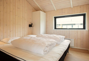 Chambre lumineuse à la maison de vacances à Sæby, Danemark, avec lit double, panneaux bois et grande fenêtre.