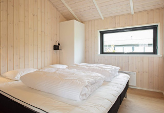 Helles Schlafzimmer im Ferienhaus in Sæby, Dänemark, mit Doppelbett, Holzverkleidung und Fenster.