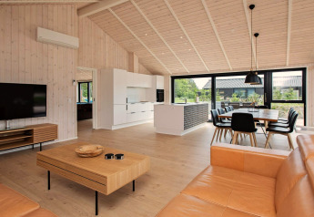 Maison de vacances moderne à Sæby, Danemark, salon, cuisine ouverte, salle à manger et grandes fenêtres.