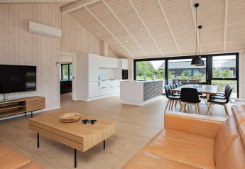 Maison de vacances moderne à Sæby, Danemark, salon, cuisine ouverte, salle à manger et grandes fenêtres.